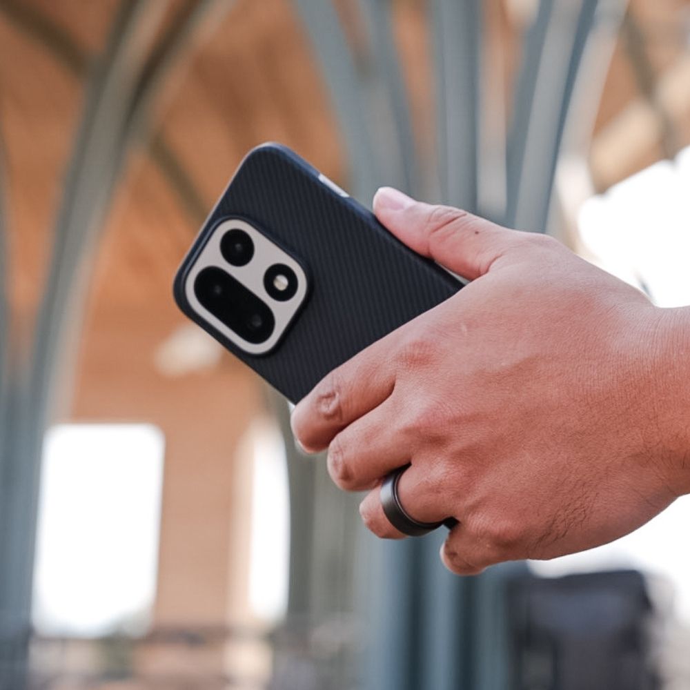 手に持った OnePlus 15 が、Thinborneの超軽量ケースによってスリムなまま保護されている様子。カーボンファイバー調のマットな質感が際立つライフスタイル写真。
