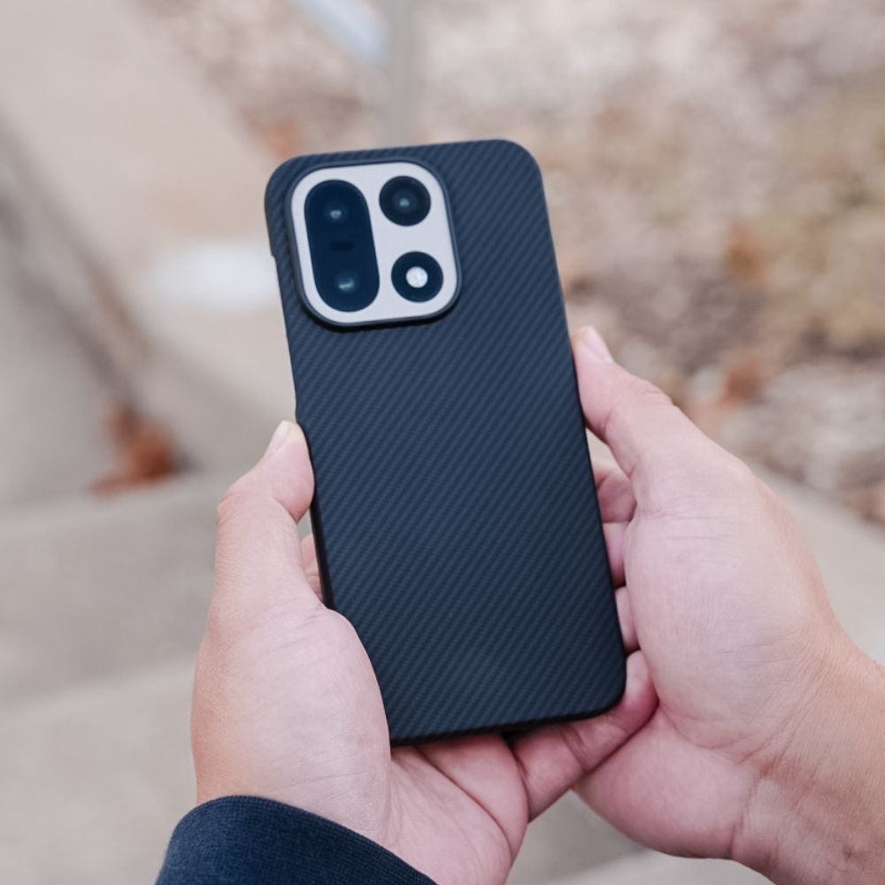 代替テキスト: 両手で保持された OnePlus 15 用ネイビー・アラミド繊維ケース。600Dアラミド素材の繊細な織り目と、カメラレンズ周辺の立ち上がりによる保護機能を示す背面ショット。