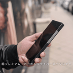 黒いカーボン調のSamsung Galaxy S25 Ultra ケースを装着したスマホを、屋外で手に持っている写真。下に「超プレミアム・カーボンファイバー調テクスチャ」と書かれています。