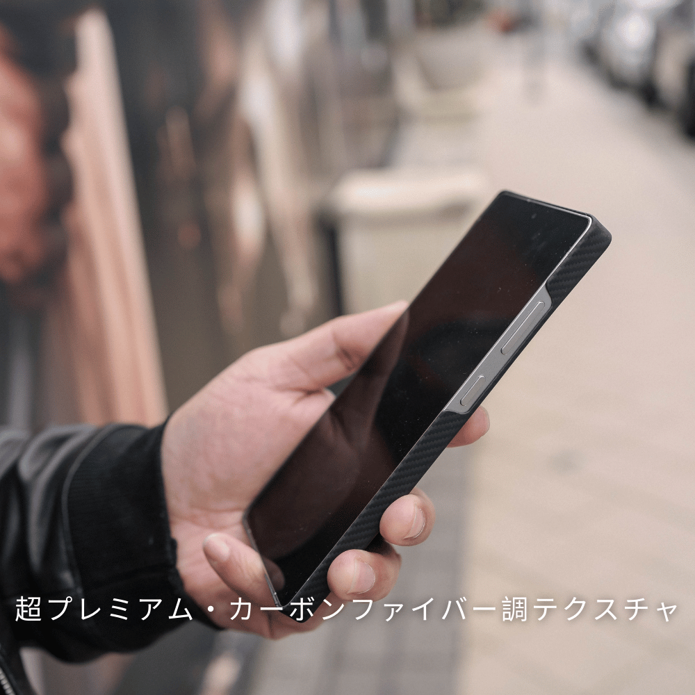 黒いカーボン調のSamsung Galaxy S25 Ultra ケースを装着したスマホを、屋外で手に持っている写真。下に「超プレミアム・カーボンファイバー調テクスチャ」と書かれています。