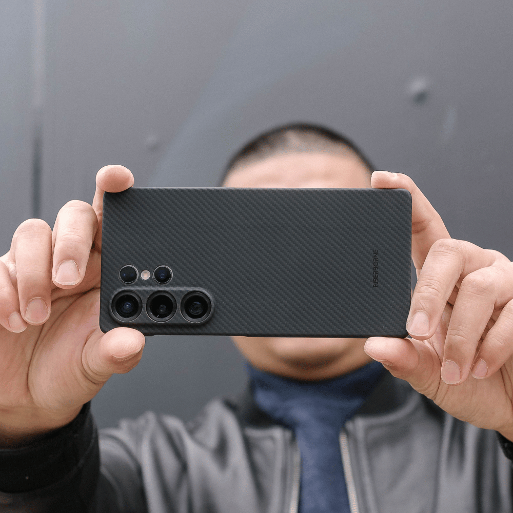 黒いカーボン調のSamsung Galaxy S25 Ultra ケースを両手で持ち、カメラを構えている人物の写真。