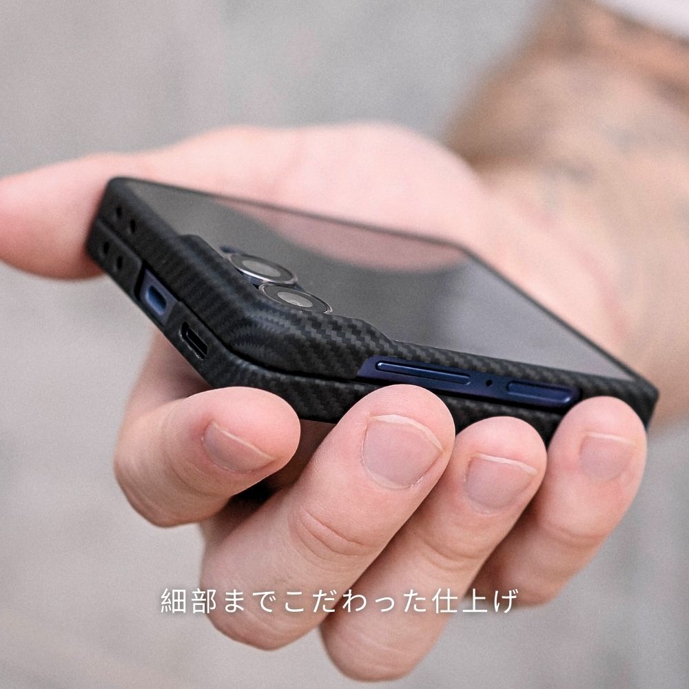 指で挟んで持った、カーボンファイバー調のGalaxy Z Flip 7 ケースを装着したスマートフォン。ケースの細部にまでこだわった作りがわかる。
