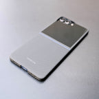 カーボンファイバー調のGalaxy Z Flip 7 ケースを装着したスマートフォンが、机の上に置かれている。閉じた状態のケース全体が写っている。

