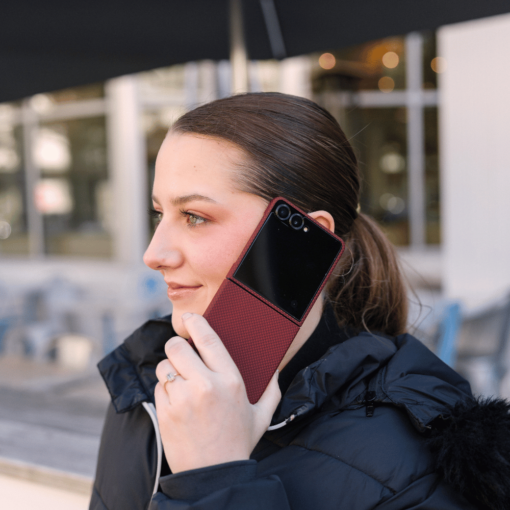 クリムゾンレッドのケースをつけたGalaxy Z Flip 8を開いて耳に当て、通話している女性の横顔。