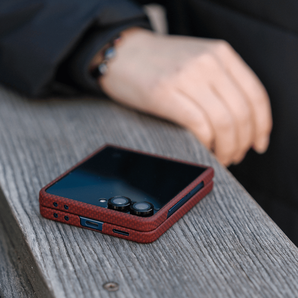 木目調のテーブルの上に折りたたんで置かれた、クリムゾンレッドのカーボン風ケース付きGalaxy Z Flip 8。