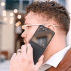 ブラックのケースをつけたGalaxy Z Flip 8を開いて耳に当て、通話している男性の横顔。