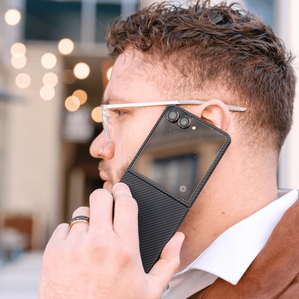 ブラックのケースをつけたGalaxy Z Flip 8を開いて耳に当て、通話している男性の横顔。
