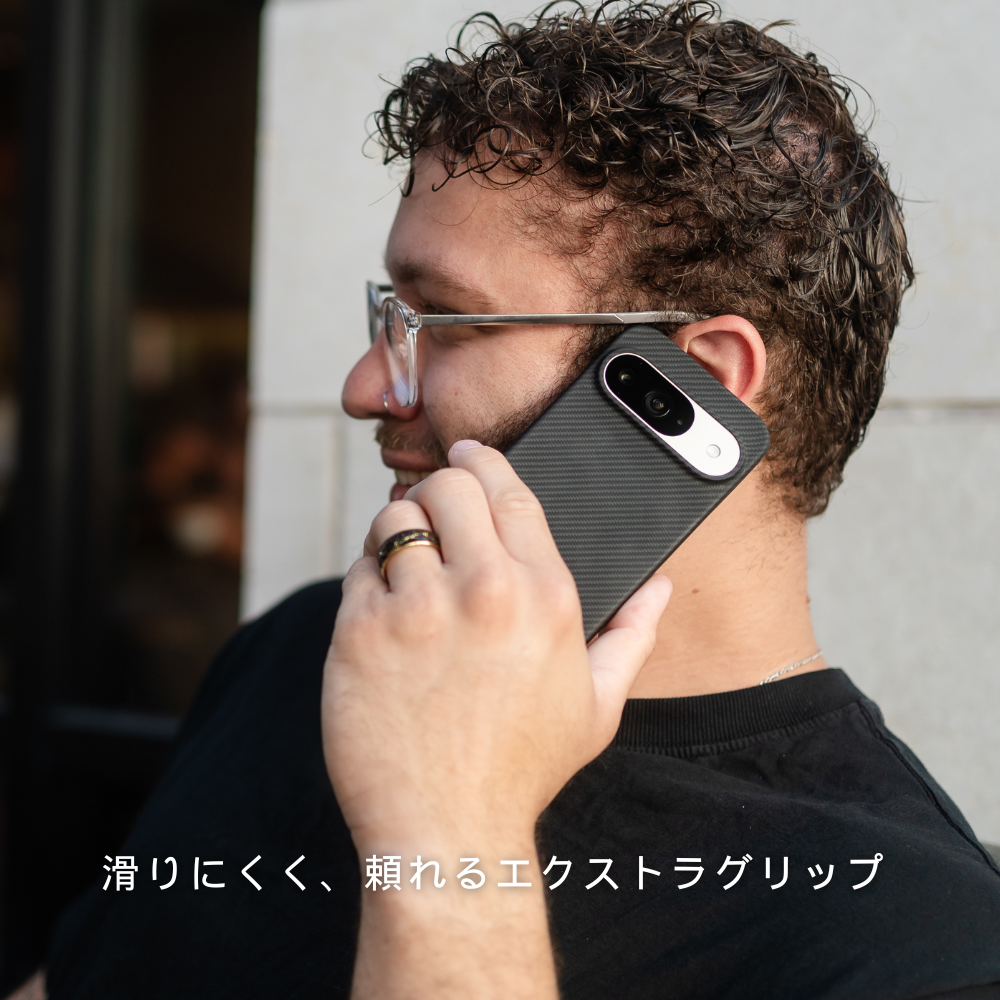 Google Pixel 10 ケースを装着したスマホで電話をする男性。ケースは滑りにくいカーボン調で、画面下に「滑りにくく、頼れるエクストラグリップ」とあります。