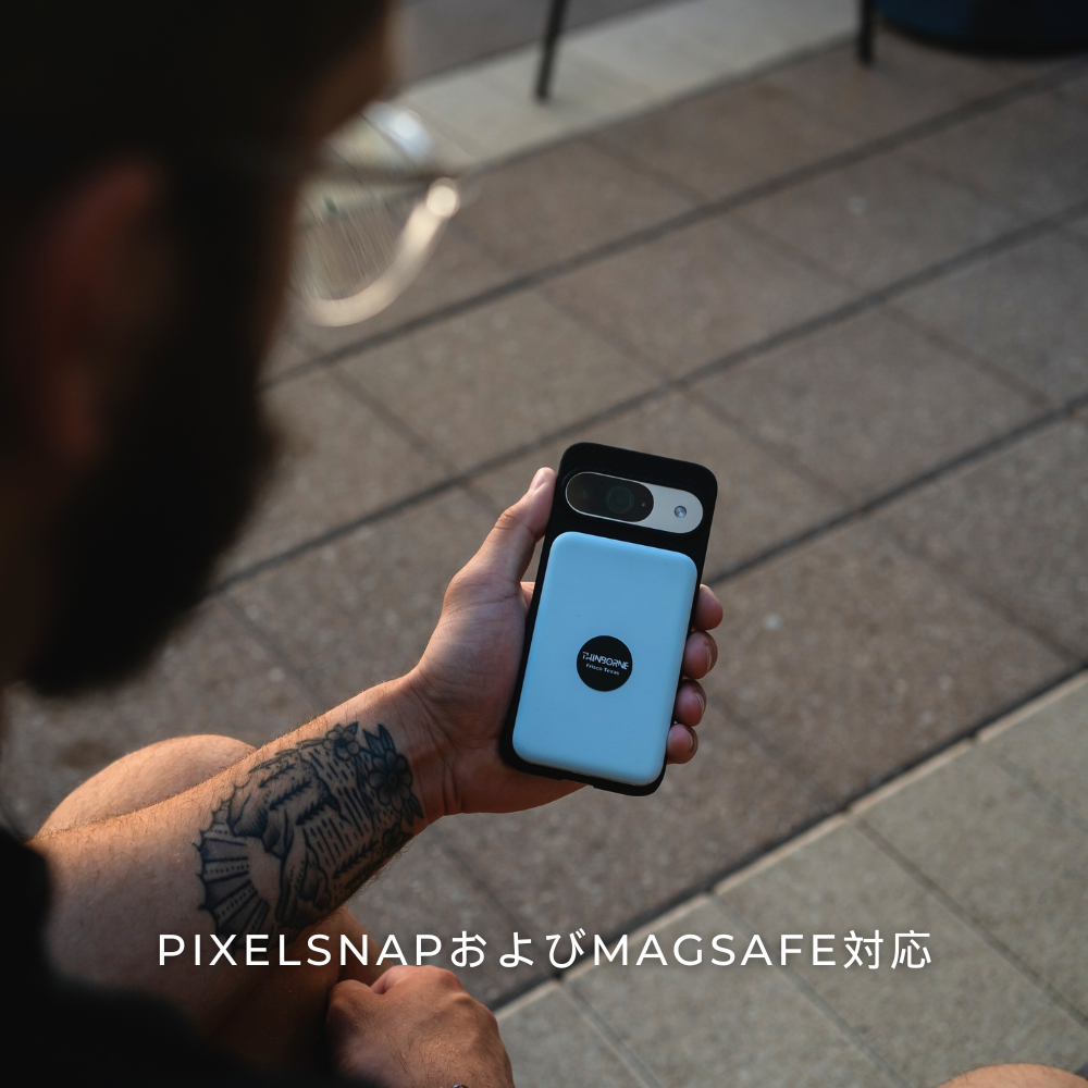 黒いケースを装着したGoogle Pixelのスマホを手にした人物。ケースには水色の長方形のMagSafe対応アクセサリーが付いており、「PIXELSNAPおよびMAGSAFE対応」と書かれています。