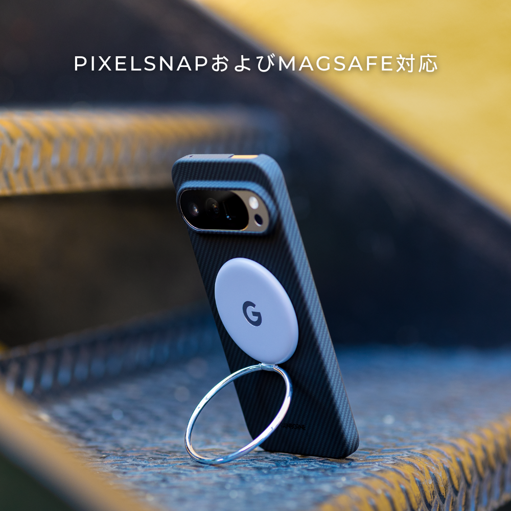黒いカーボン調のGoogle Pixel 10 ケース。MagSafe対応の白いアクセサリーとリングスタンドで、階段に立てかけられています。上部に「PIXELSNAPおよびMAGSAFE対応」の文字。